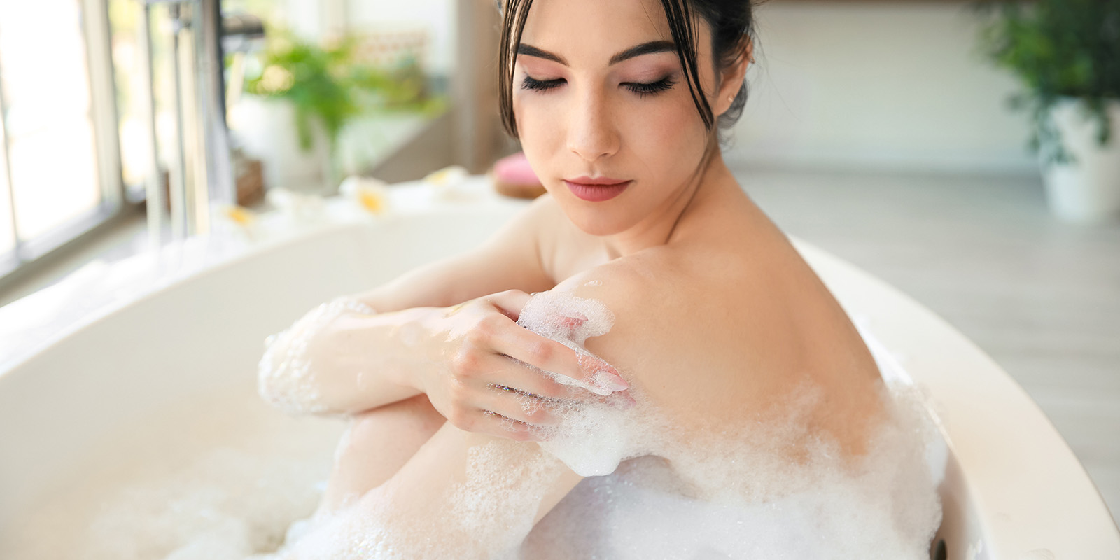 Eine hübsche Frau sitzt in einer Badewanne mit viel Schaum und streicht sich über die Schulter.